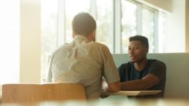 Aman and a young employee talking at a table in an office