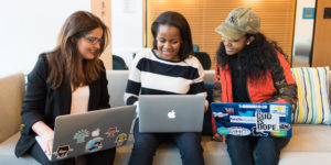 3 young people on work experience, looking at their laptops while sitting on a sofa in an office