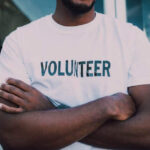 a man taking time out of work to volunteer, standing in a T shirt with the word 'volunteer' written on it.