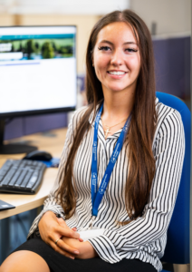 A image of Blossom, a worker at Buckinghamshire Council sat at her desk on a blue computer chair.